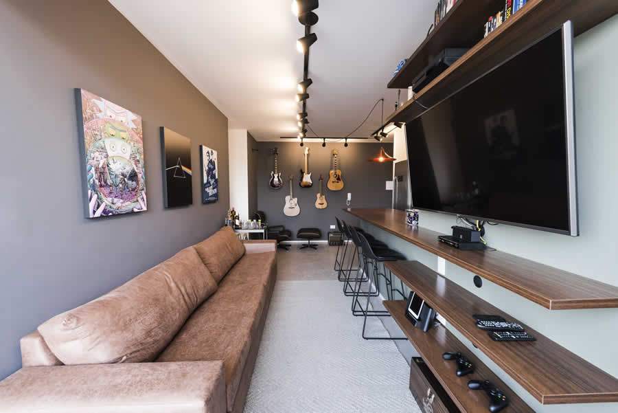 A sala de estar adota uma paleta de tons marrom, preto e cinza, enquanto incorpora os gostos pessoais do morador, com instrumentos musicais integrados à decoração industrial | Projeto da Panapaná Estúdio de Projetos | Foto: Rafael Roncato