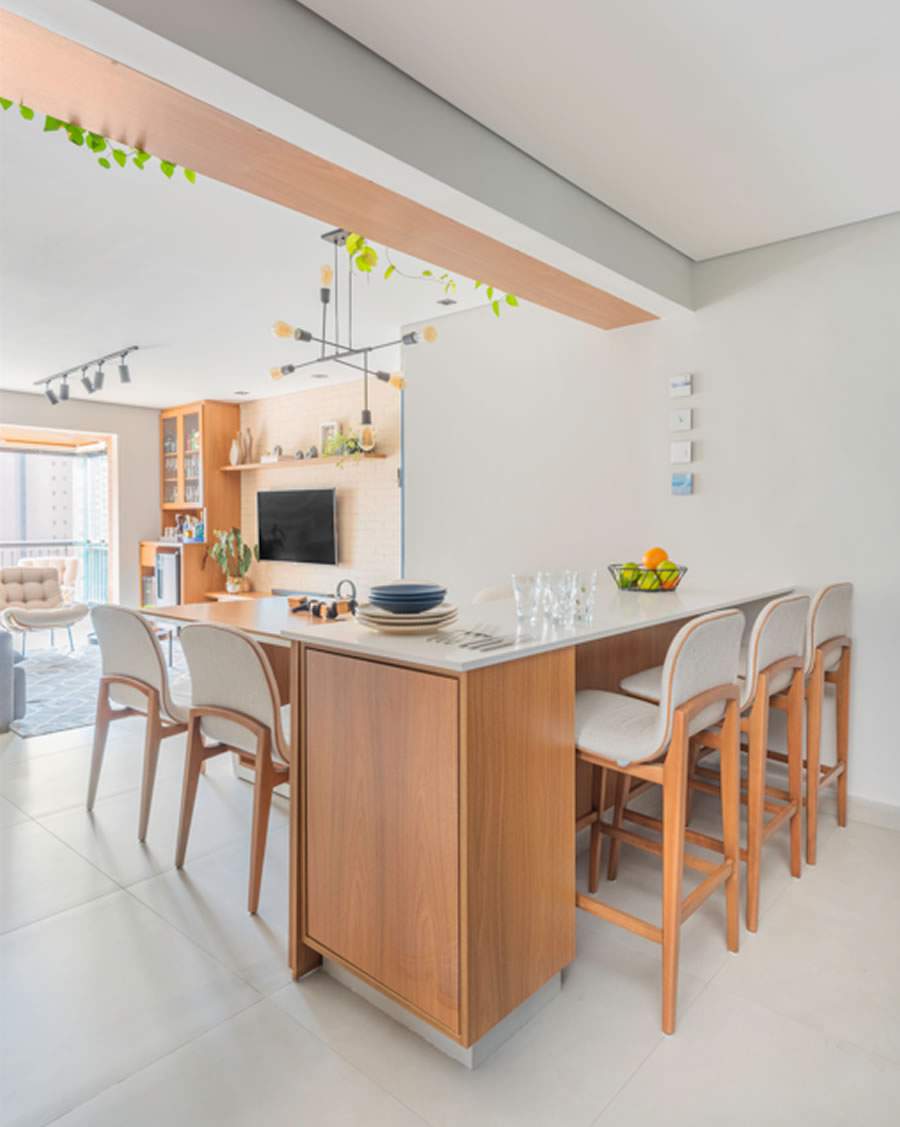 Em alta na decoração, a bancada do tipo ilha, presente em cozinhas e varandas gourmet, é a perfeita combinação com as banquetas altas. Neste apartamento, o arquiteto Bruno Moraes elegeu móveis com assento e estrutura de madeira arredondadas | Foto: Guilherme Pucci