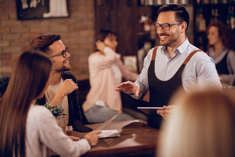 smiling-waiter-holding-digital-tablet-while-taking-order-from-couple-bar